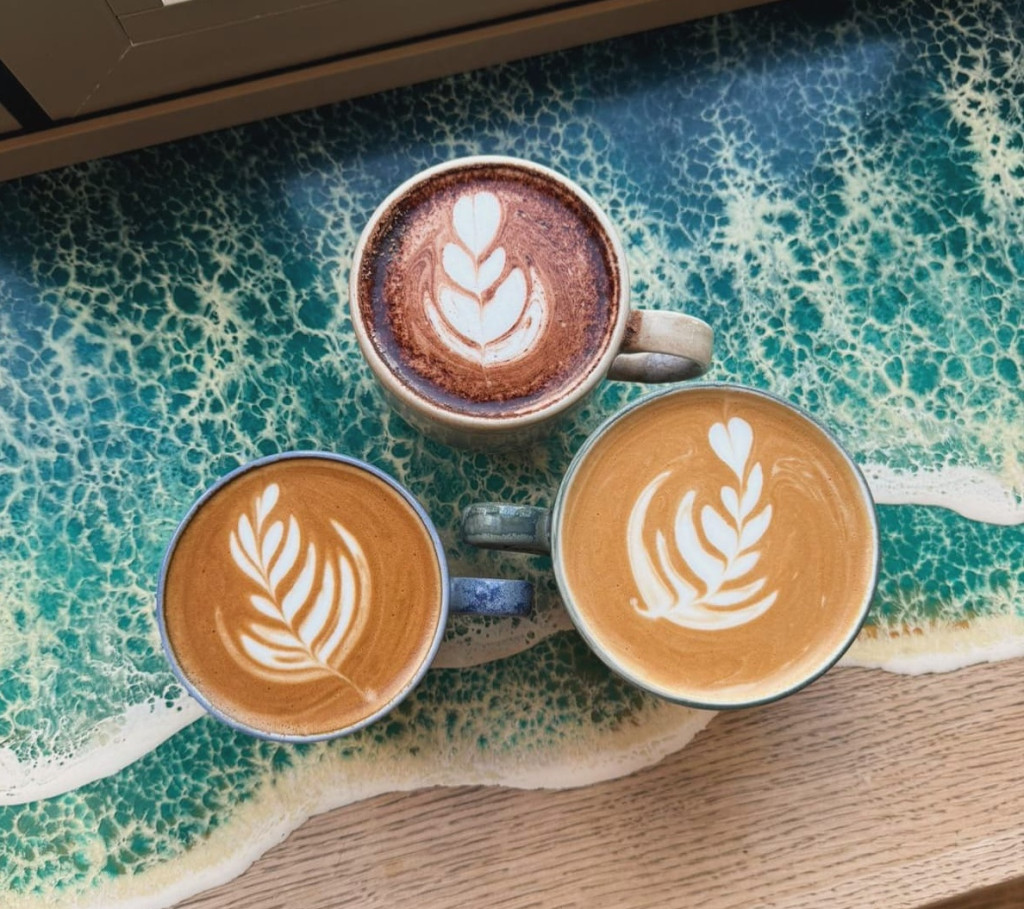 Three cups of coffee with leaf latte art are arranged on a table with an ocean-inspired blue and white pattern.