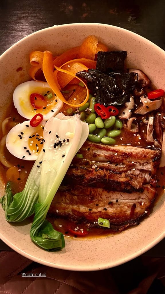 A bowl of ramen with pac choi, an egg, carrot and meat.