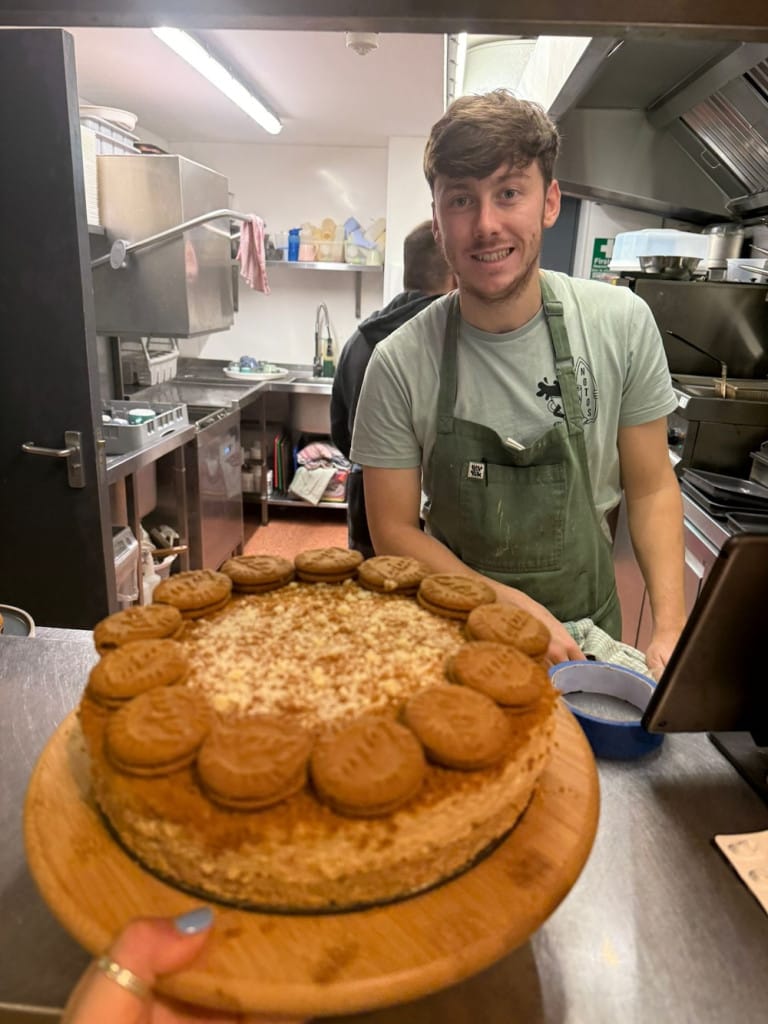Someone holds a birthday cake up to the chef that made it in a cafe kitchen