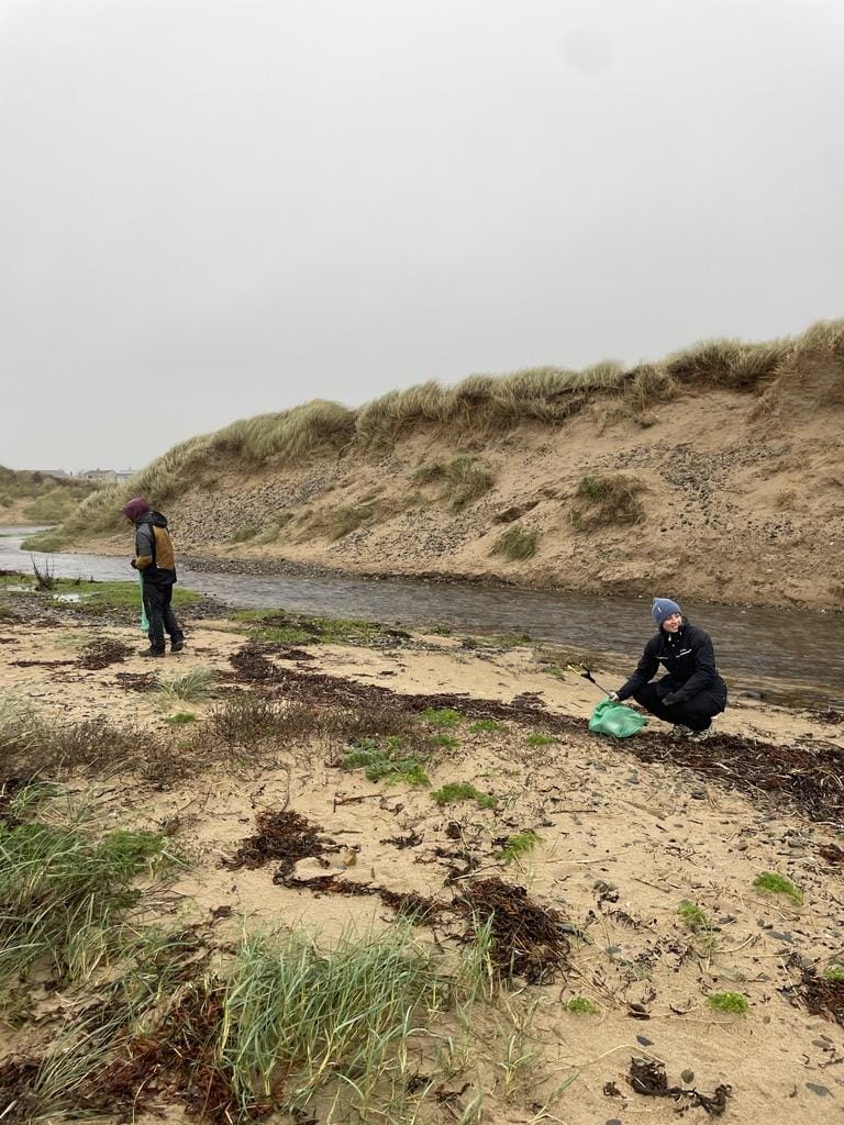 Two people collecting litter at the beach in rainy weather
