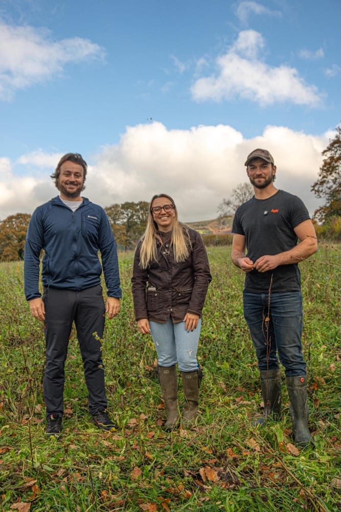 three people standing in a grassy field smiling at the camera