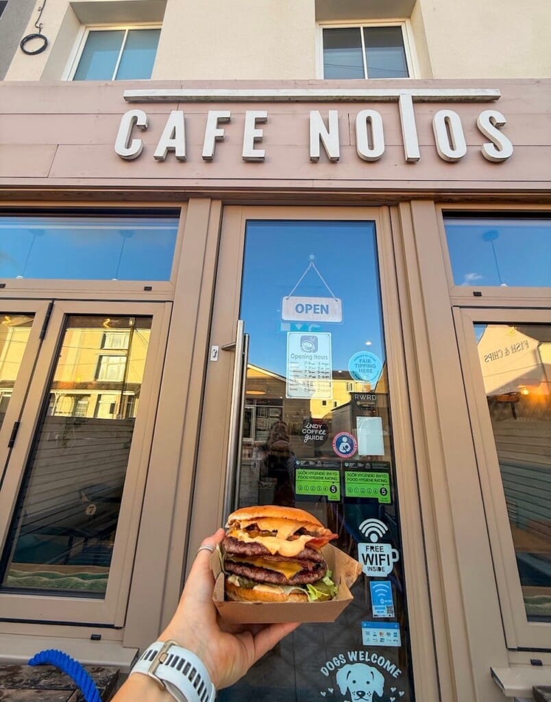 A burger in a takeaway box held up to the café front door