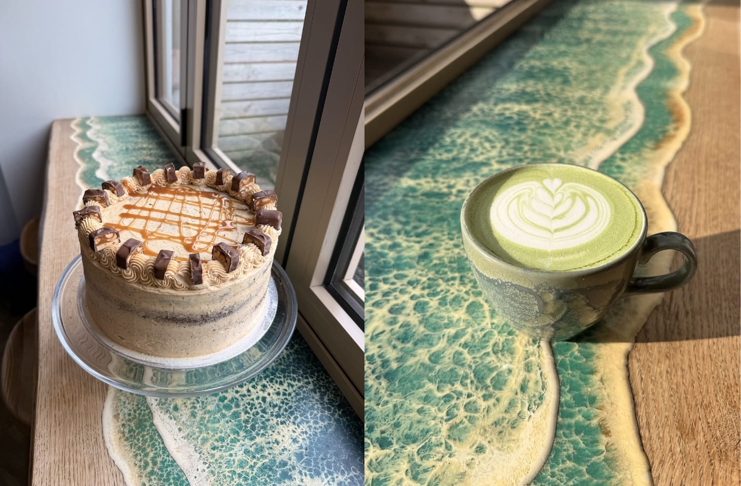 A caramel cake on a glass stand and a cup of matcha latte with latte art sit on a wooden table with an ocean-like resin design by a window.